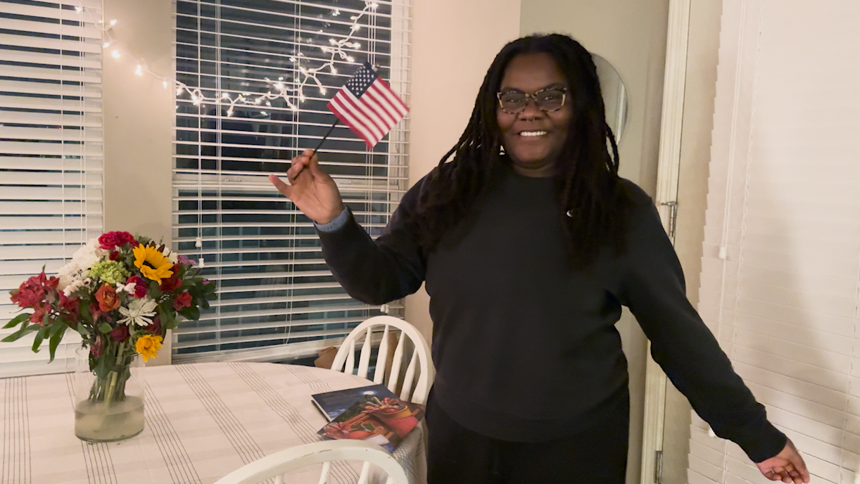 A woman holds a small American flag and smiles.